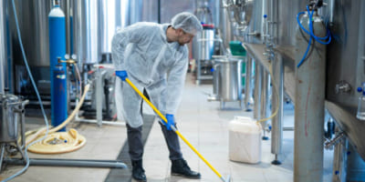 Professional industrial cleaner in protective uniform cleaning floor of food processing plant. Cleaning services.